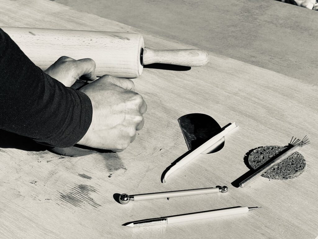 Zwei Hände formen weichen Ton an einem Arbeitstisch im Atelier Lehmtanz als Symbol für die kreativen Töpferkurse für Anfänger und Fortgeschrittene.
